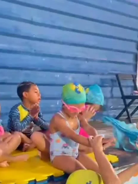 Bebês sentados na borda da piscina com materiais coloridos