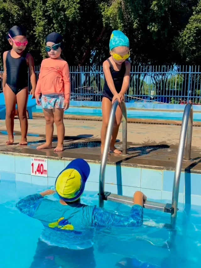 Crianças em pé na borda da piscina antes de começar a aula